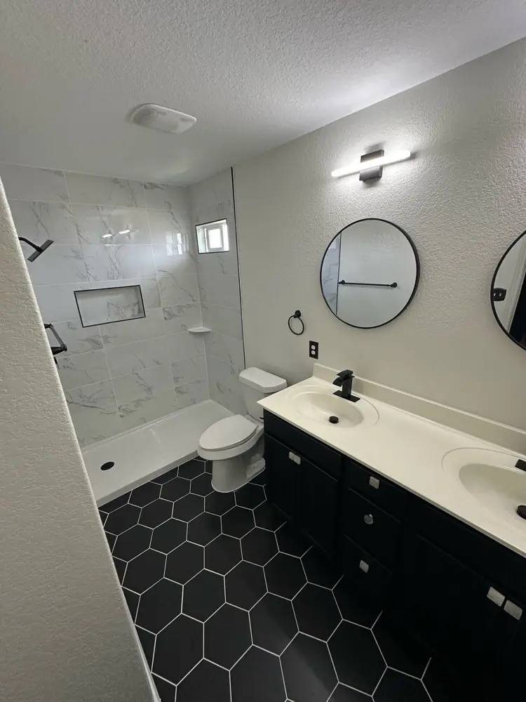Finished bathroom with marble-look shower and black hex tile floor