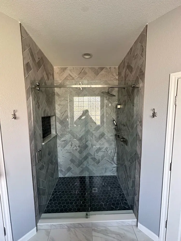 Finished walk-in shower — herringbone tile and frameless glass